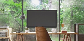 Ein Monitor auf einem Schreibtisch, im Hintergrund ist ein Wald zu sehen
