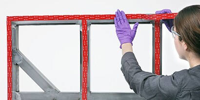 Technikerin beim Anbringen eines Industrieklebebands auf einen Rahmen zur Montage einer Platte
