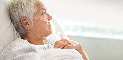 Ältere Frau in einem Krankenhausbett, die aus dem Fenster sieht.
