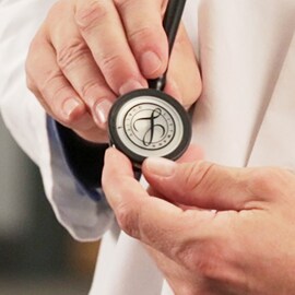 Nahaufnahme eines Arztes, der das Bruststück eines 3M Littmann Stethoskops mit dem Littmann Logo auf der Membran hält.