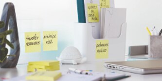 Auf dem Schreibtisch stehen ein Notizbuch, ein Laptop und Super-Haftnotizen.
