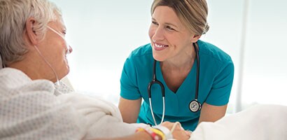 Ärztin mit Stethoskop, die die Hand einer älteren Patientin hält.
