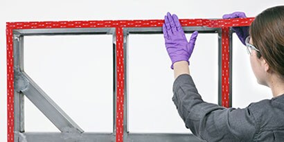 Person, die ein VHB Klebeband an einem Rahmen zur anschließenden Montage einer Platte anbringt
