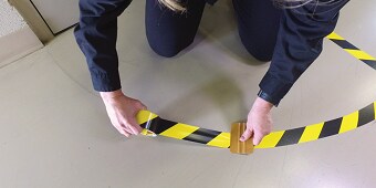 Bild einer Person, die eine gelb-schwarze Warnmarkierung auf den Boden anbringt
